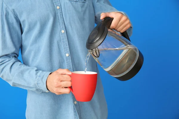 Young Man Pouring Water Electric Kettle Cup Color Background — Stock Photo, Image