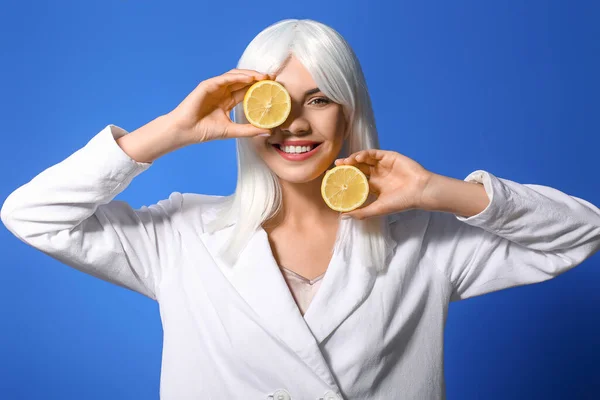 Beautiful young woman in wig and with lemon on color background
