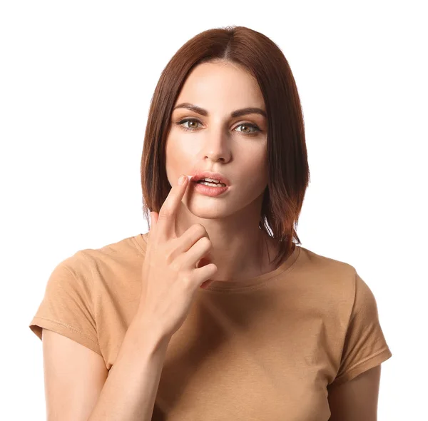 Young woman with cold sore applying ointment on her lips against white background