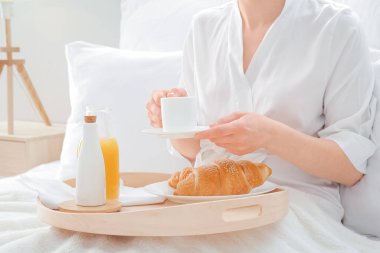 Genç bir kadın otel odasında yatakta kahvaltı yapıyor.