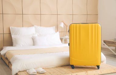 Otel odasında yatağın yanındaki bavul.