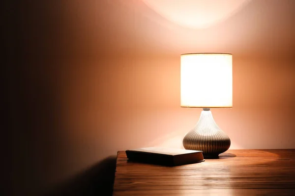 Glowing lamp with book on table in evening