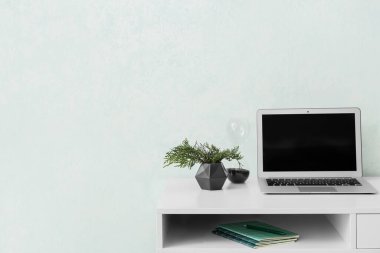 Oda beyaz duvarın yanında dizüstü bilgisayarı olan bir masa.