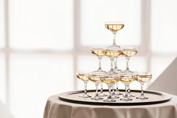 Tower made of glasses with champagne on table indoors