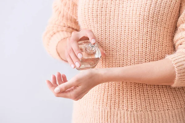 Young woman with perfume on light background, closeup