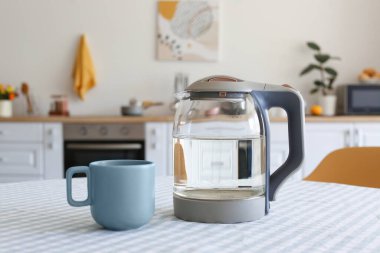 Elektrik ısıtıcısı ve bardak mutfak masasında.