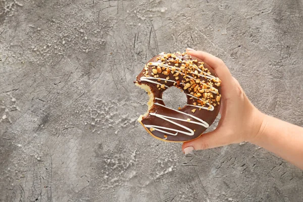 Hand with sweet bitten donut on grey background