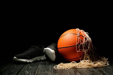 Ball for playing basketball, shoes and net on table against dark background clipart