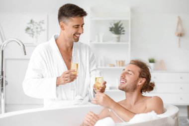 Mutlu eşcinsel çift banyoda şampanya içiyor.