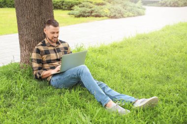 Bilgisayarlı yakışıklı adam parkta dinleniyor.