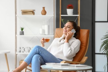 Evde telefonla konuşurken çay içen güzel genç bir kadın.