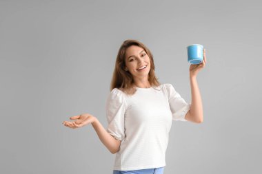 Gri arka planda bir fincan çayı olan güzel genç bir kadın.