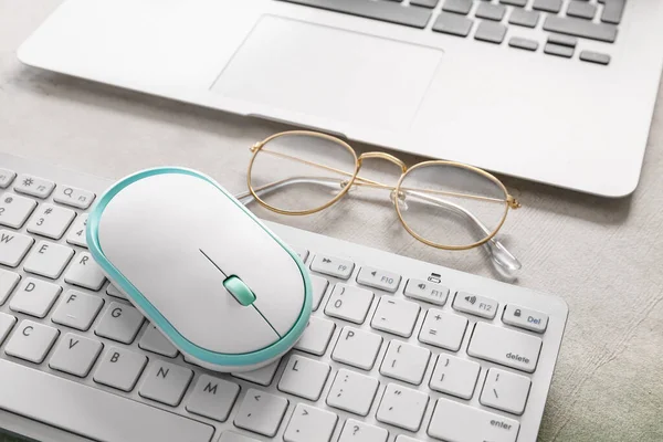 Modern PC mouse, keyboard and glasses on table