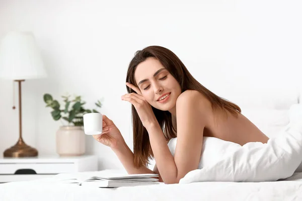 Seductive woman drinking coffee and reading book in bed at home