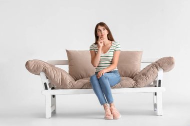 Düşünceli genç bir kadın modern koltukta, arka planda.