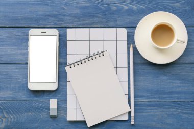 Cep telefonlu defterler ve renkli ahşap arka planda bir fincan kahve.