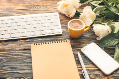 Cep telefonu, bilgisayar klavyesi ve ahşap arka planda bir fincan kahve olan defter.