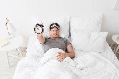 Çalar saati olan stresli adam yatak odasında uykusuzluk çekiyor.