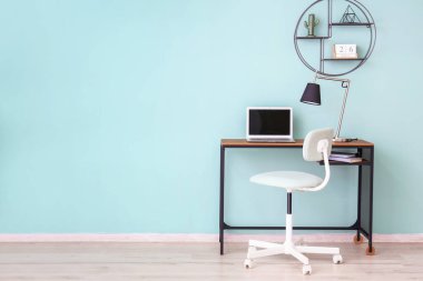 Dizüstü bilgisayarlı masa ve renkli duvarın yanındaki sandalye.