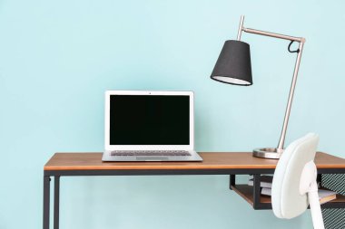 Renkli duvarın yanında dizüstü bilgisayarı ve lambası olan masa