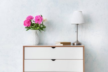 Modern çekmeceler lamba ve çiçeklerle aydınlık duvarın yanında.