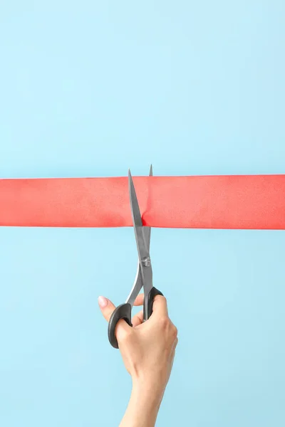 Woman cutting red ribbon on color background