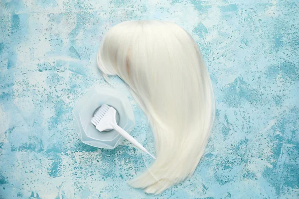 Unusual wig with supplies for hair dyeing on color background