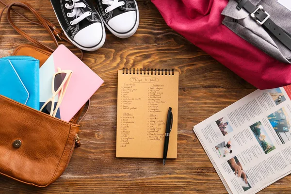 Notebook with check-list of things to pack for travel on wooden background