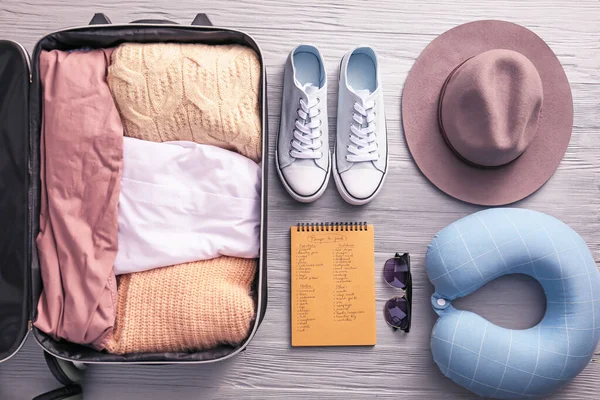 Notebook with things to pack for travel on wooden background