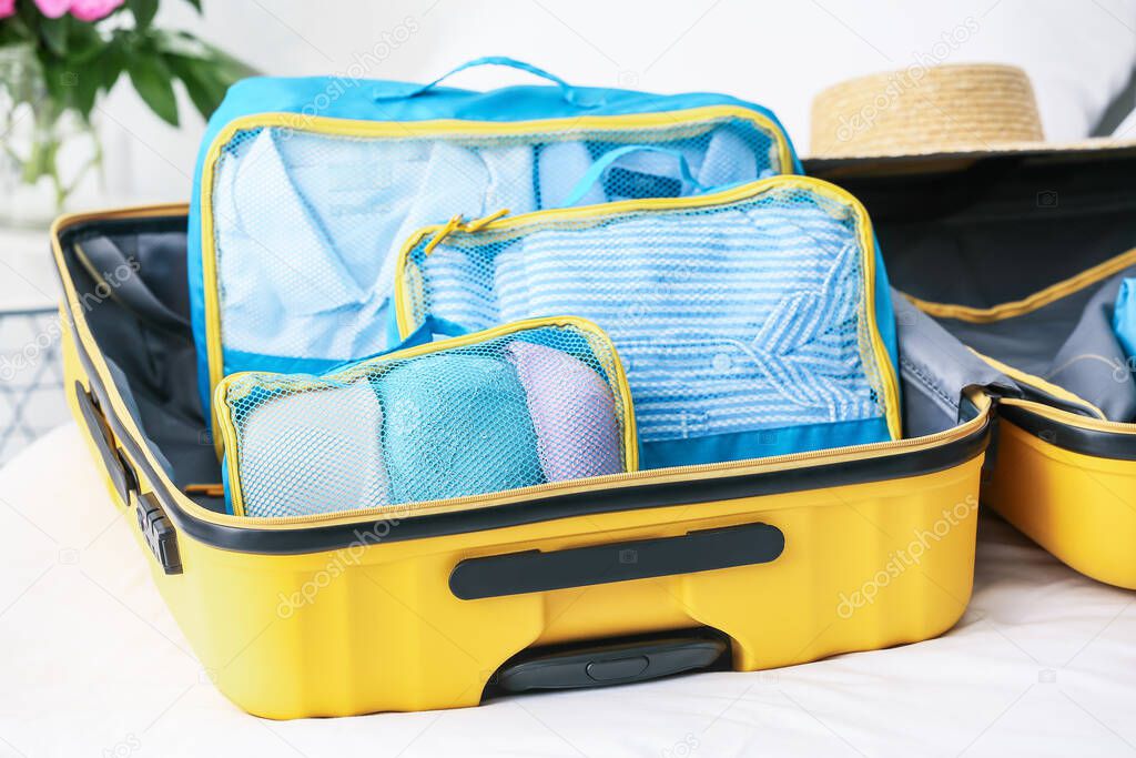 Suitcase and set of travel organizers with belongings on bed at home