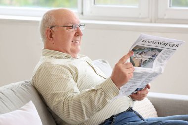 Evde gazete okuyan kıdemli bir adam.