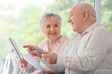 Evde tablet bilgisayarı ve kredi kartı olan yaşlı çift.