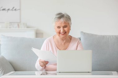 Evde dizüstü bilgisayarı olan yaşlı bir kadın.