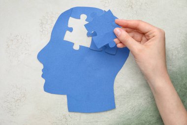 Kağıttan insan kafasıyla kadın eli ve arka planda yapboz parçaları. Nöroloji kavramı