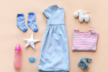 Şişeli bebek kıyafetleri, emzik ve renkli arka planda oyuncaklar