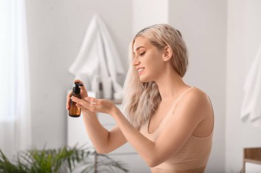 Güzel genç bir kadın banyoya kozmetik yağı sürüyor.