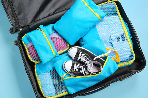 Suitcase and set of travel organizers with belongings on color background