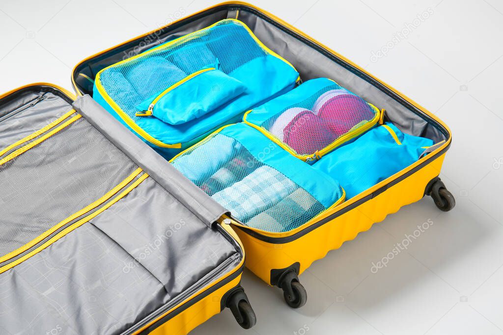 Suitcase and set of travel organizers with belongings on white background