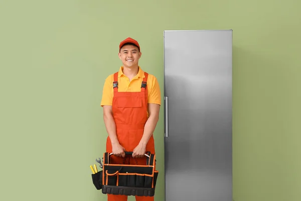 Worker of repair service near fridge on color background