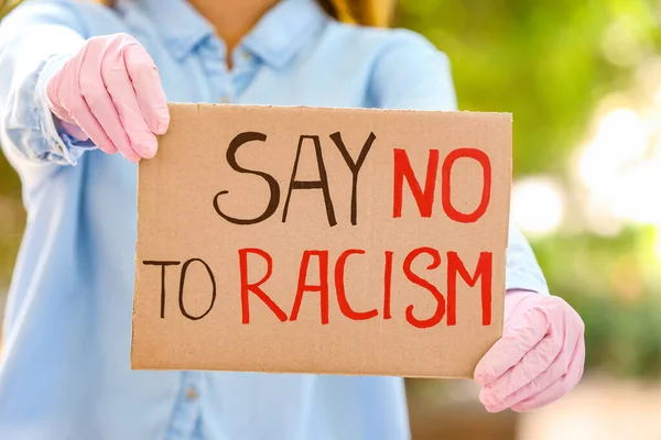 Woman holding poster with text SAY NO TO RACISM outdoors, closeup