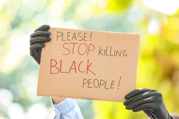 Woman holding poster with text PLEASE STOP KILLING BLACK PEOPLE outdoors