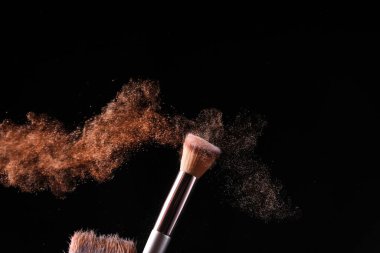 Koyu arkaplanda makyaj fırçası ve kozmetik patlaması