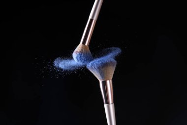 Koyu arkaplanda makyaj fırçaları ve kozmetik patlamaları