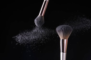 Koyu arkaplanda makyaj fırçaları ve kozmetik patlamaları