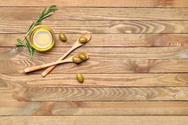 Bir kase zeytinyağı ve tahta arka planda kaşıklar.