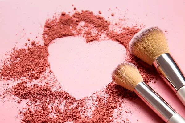 Makyaj fırçaları ve renk arkaplanındaki kozmetikten yapılmış kalp