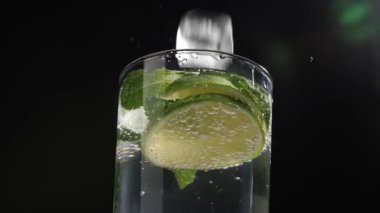 Koyu arkaplanda taze mojito bardağına düşen buz küpü, yakın plan.