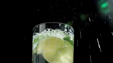 Koyu arkaplanda taze mojito bardağına düşen buz küpleri.