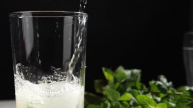 Koyu arkaplanda camla taze mojito dökülüyor.