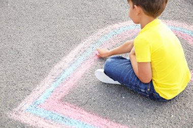 Küçük çocuk asfalta tebeşirle kalp çiziyor.